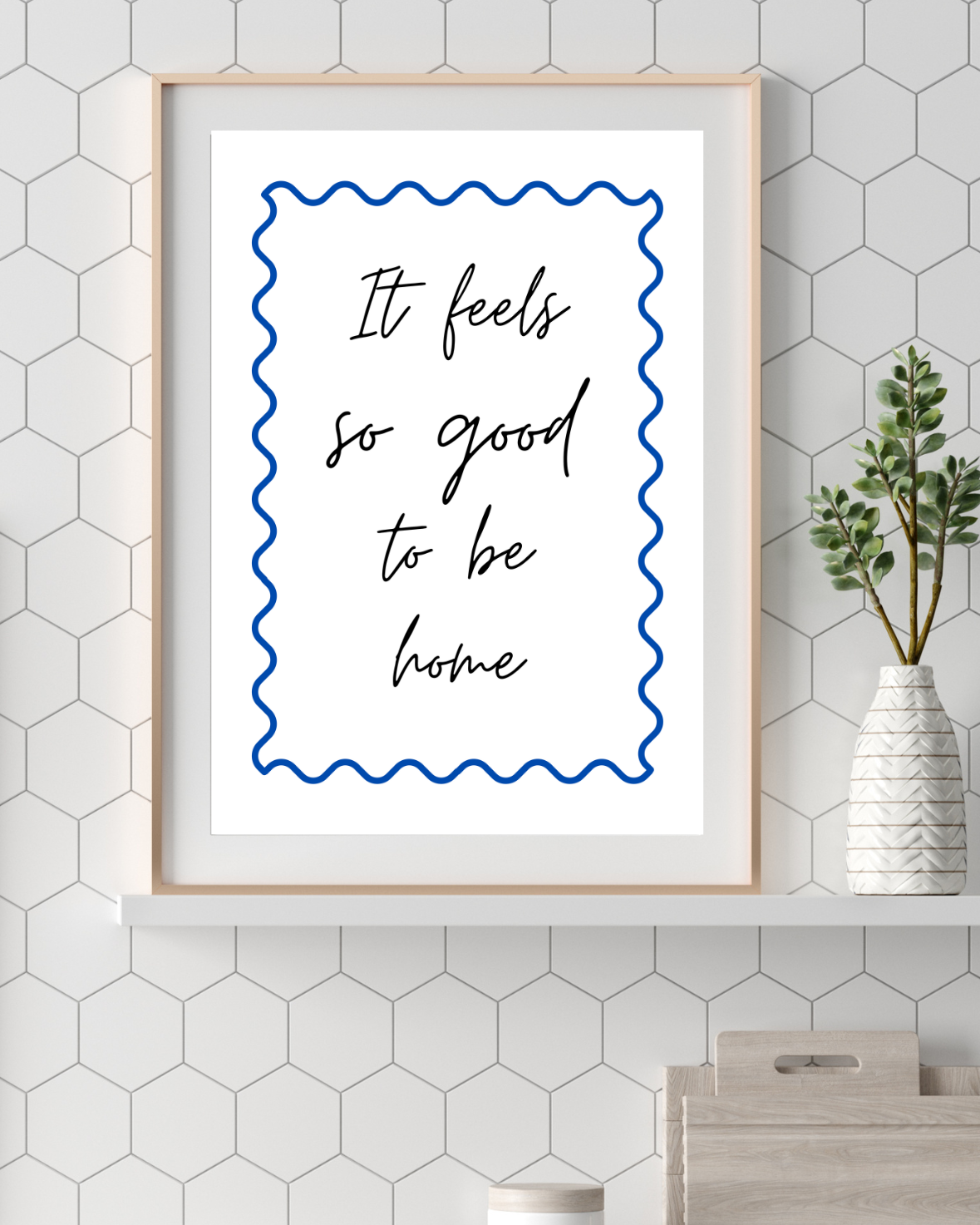 Framed print with 'It feels so good to be home' text on a hexagonal tiled wall.