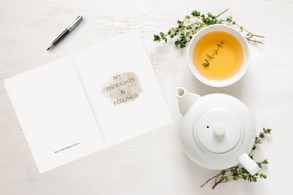 My Thoughts & Feelings journal on a wooden table beside a cup of herbal tea — a calming setup for soft life journaling, reflection, and self-care.

