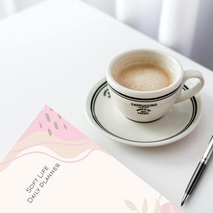 Soft Life Daily Planner for for women on a table with a cup of cappuccino.